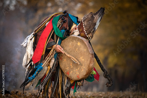 Mongolian traditional shaman performing a traditional shamanistic ritual with a drum and smoke in a forest during autumn afternoon. Ulaanbaatar, Mongolia. photo