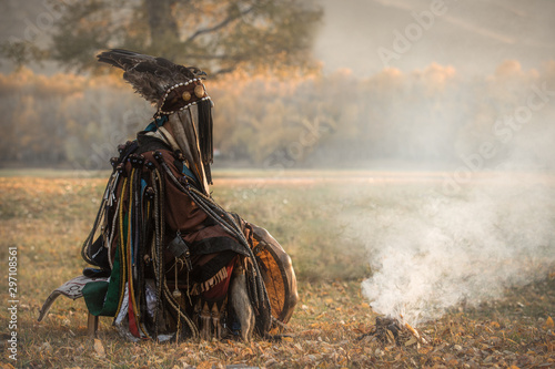Mongolian traditional shaman performing a traditional shamanistic ritual with a drum and smoke in a forest during autumn afternoon. Ulaanbaatar, Mongolia.