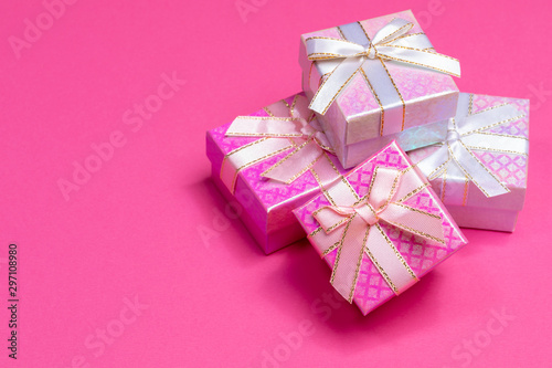 Fototapeta Naklejka Na Ścianę i Meble -  Heap of shiny gift boxes with ribbons and bows on bright pink background with copy space. 