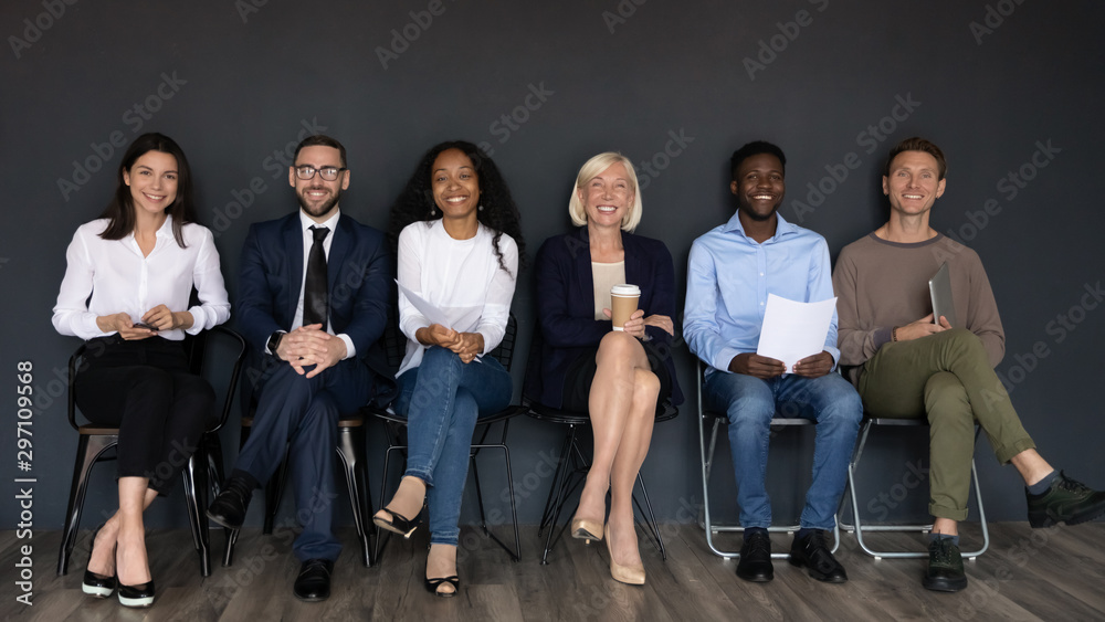 Smiling multiethnic professionals sit on chairs looking at camera