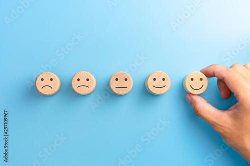Customer service evaluation and satisfaction survey concepts. The client's hand picked the happy face smile face icon on wooden cube on blue background. copy space