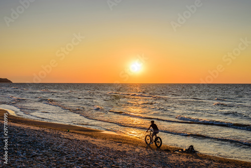 Fototapeta Naklejka Na Ścianę i Meble -  Beautiful sunset on the sea. Baltic sea at sunset, Toila, Estonia. Toila - seaside resort and popular holiday destination in Estonia. Cyclist on the beach.