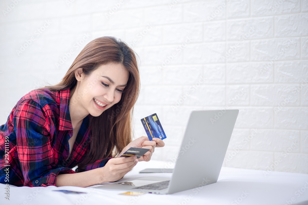 A beautiful Asian woman using a credit card and a laptop for online shopping in a private office with a smile / feel refreshed and happy in the morning.