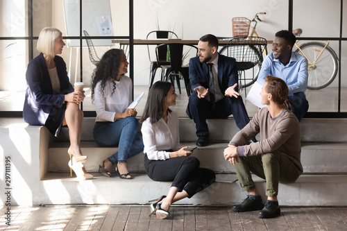 Happy multiracial business people communicating sit on modern office floor