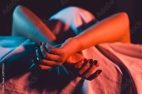 Close up on female young woman's girl's beautiful hands with black nail polish in dark room crossed fingers on the bed sheet gentle passion love temptation emotion love concept photo