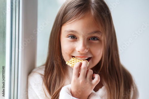 Cute little girl sitting on the window  and eating cookie aat home