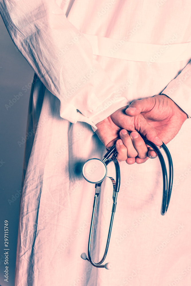 Doctor in white coat holds hands behind his back with stethoscope. Toned. Doctor in white coat holds hands behind his back with stethoscope. Toned.