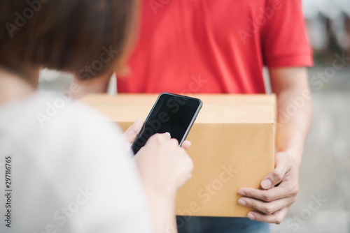 Young Asia woman digital sign technology on smartphone receiving parcel cardboard box from post man at outdoor of home which smiling and felling happy,delivery man express shipping a goods to customer