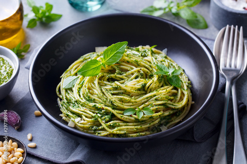 Pasta spaghetti with pesto sauce and fresh basil leaves in black bowl. Grey background. Close up.