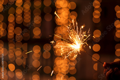 Burning Sparkler Diwali Background Image. Diwali holiday greetings card, postcard. A young woman holding lighted fireworks with bright golden Christmas bokeh lights. Background image for Diwali, x-mas