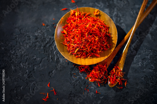 Fototapeta Naklejka Na Ścianę i Meble -  Saffron Spice. Saffron spices on black stone table in a wood bowl and a spoon. Spice and herbs on slate background. Seasonings, condiments. Cooking ingredients, flavor