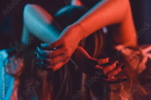 Close up on female young woman's girl's beautiful hands woman lying on the bed with black nail polish in dark room crossed fingers on sheet gentle passion love temptation emotion concept photo