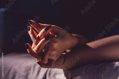 Close up on female young woman's girl's beautiful hands with black nail polish in dark room holding crossed fingers on the bed sheet gentle passion love temptation emotion love concept