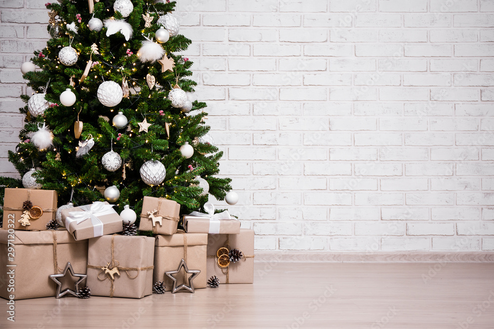 decorated christmas tree and gift boxes over white brick wall with copy space - obrazy, fototapety, plakaty 