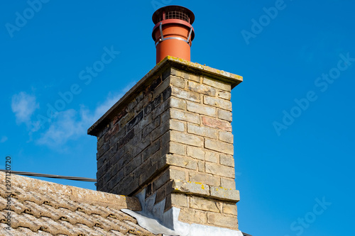 Large, english cottage style brick chimney showing a newly installed terracotta pot together with a chimney cover to prevent birds nesting. Part of the roofing can also be seen. photo