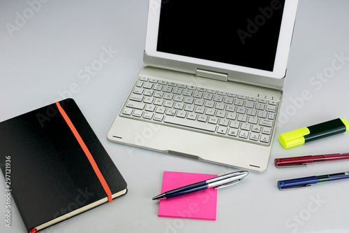 Office supplies consisting of tablet with keyboard, fluorescent marker, red and blue markers, modern pen, sticky notepad and note book photo