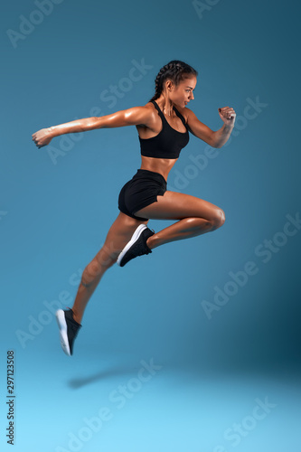 professional athlete training at sport center, full length side view photo. isolated blue background, studio shot.health and body care, wellness, woman is running to her dream