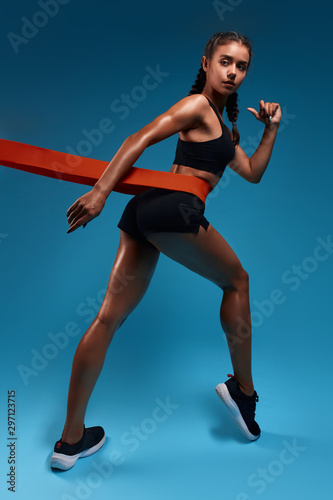 slim tanned sweaty girl concentrated on training, breaking record, is being keen on sport. full length photo. isolated blue background, studio shot.