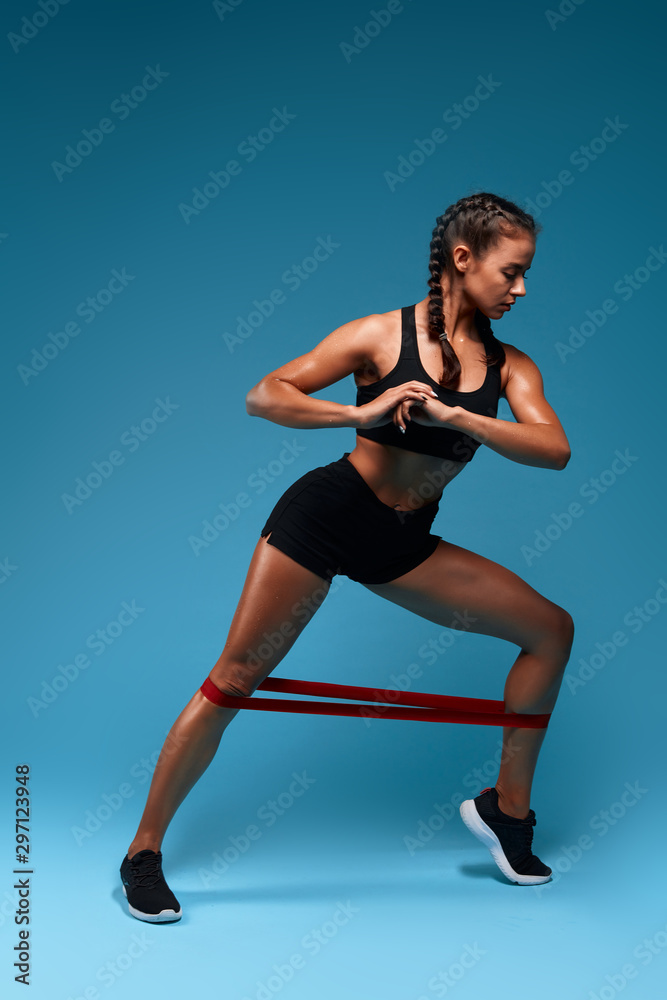 serious girl using expander to perform lunge, full ength photo. isolated blue background, studio shot.free time, spare time, lifestyle
