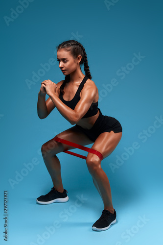 Attractive beautiful motivated sportswoman doing sit-ups with expander .professional trainer instructor, full length side view photo. isolated blue background, studio shot.