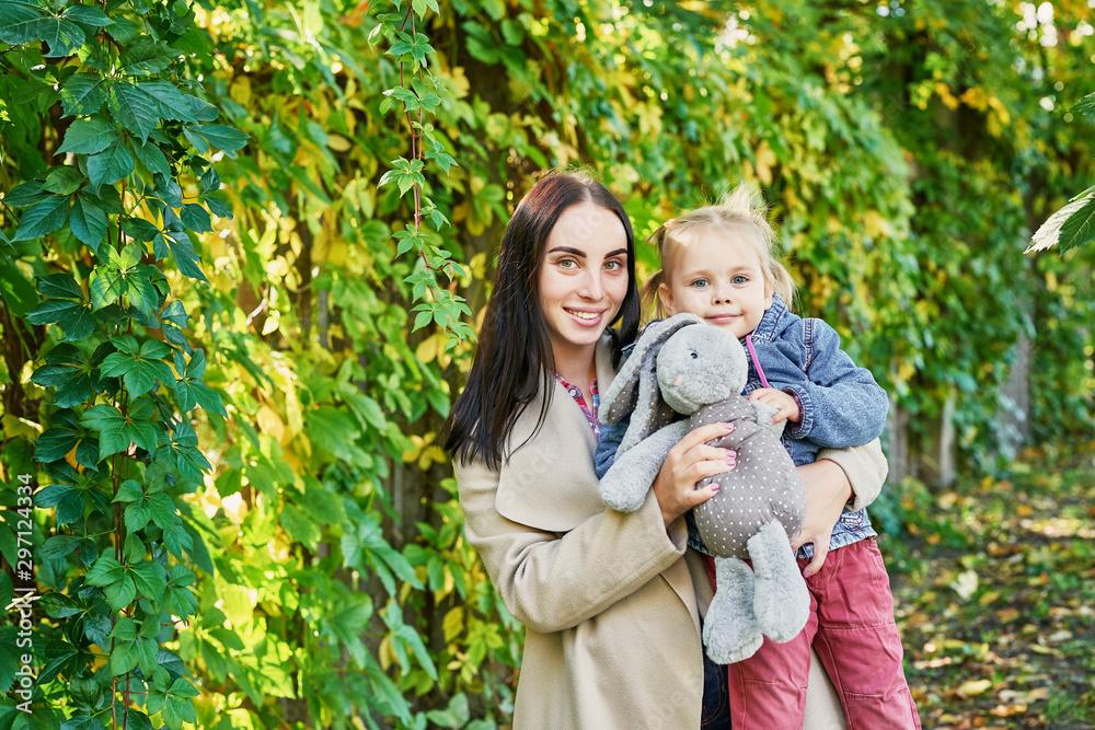 Fototapeta premium Happy family on autumn walk. Mother and daughter walking in Park and enjoying beautiful autumn nature. Hello, Autumn! Happy loving family having fun. Autumn leaf fall