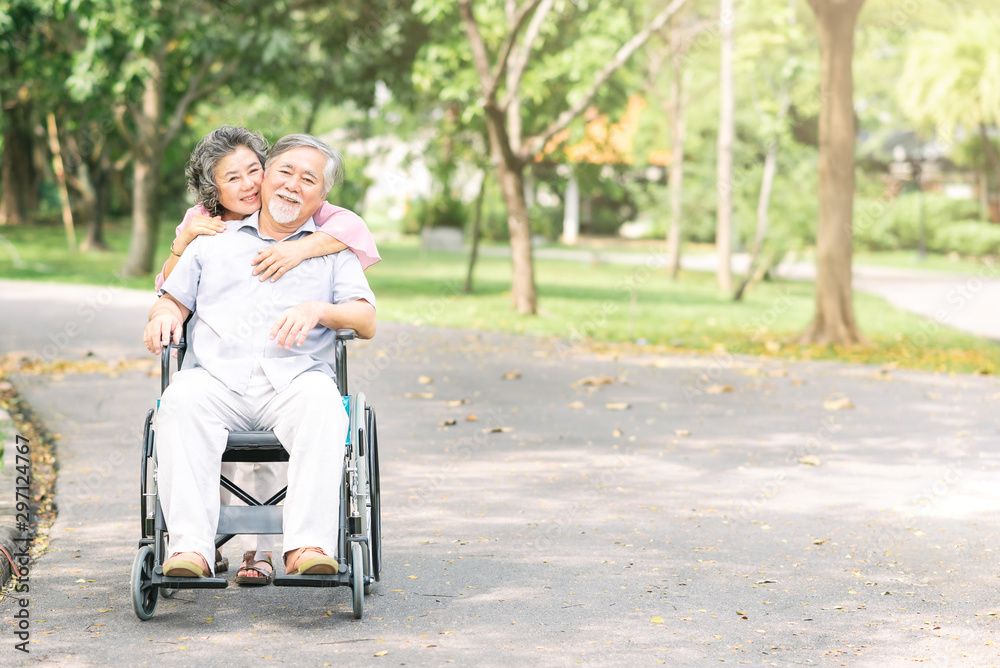 senior woman hugging her husband in wheelchair from behind senior woman hugging her husband in wheelchair from behind