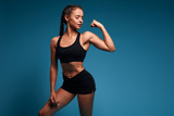 pretty sexy slim attractive girl in fashion bra and shorts shows her biceps. close up photo. isolated blue background, studio shot. copy space. strength training, health and body care