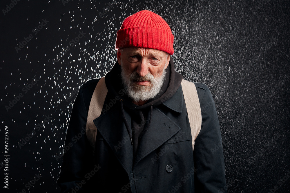 Bearded old man wearing black street clothes and holding iron cup for money, for help. Sad homeless man under heavy rain. Bearded old man wearing black street clothes and holding iron cup for money, for help. Sad homeless man under heavy rain.