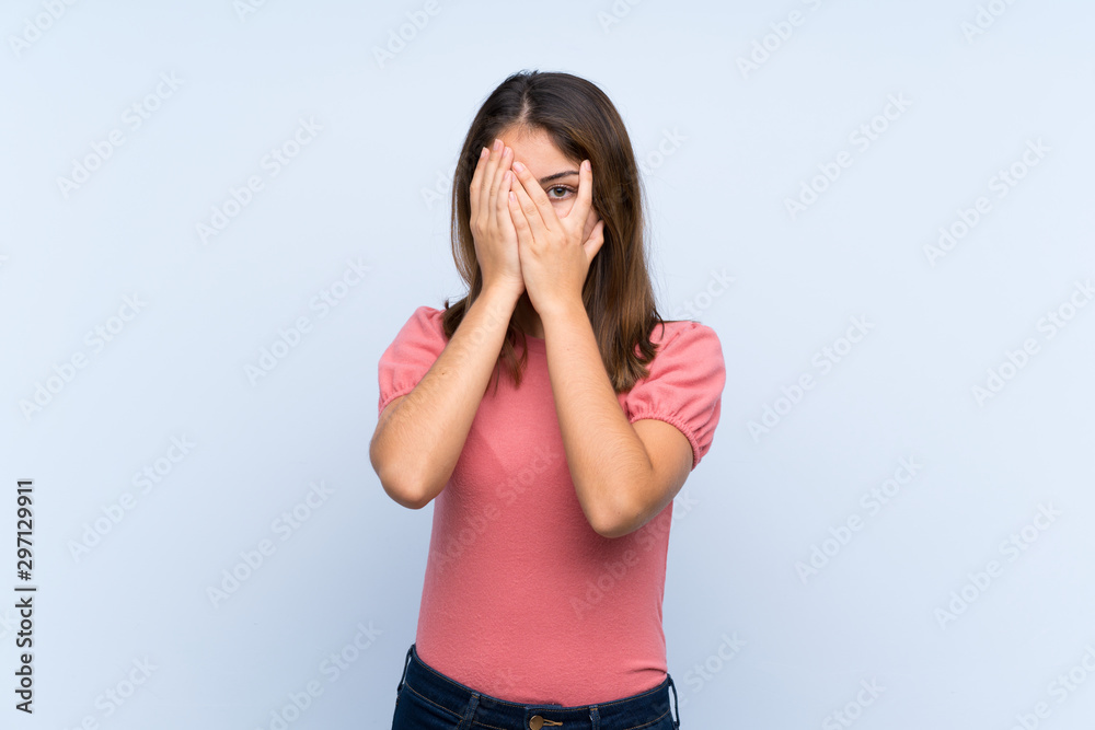 Young brunette girl over isolated blue background covering eyes and looking through fingers Young brunette girl over isolated blue background covering eyes and looking through fingers
