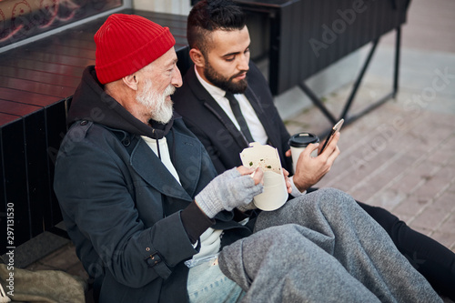 Handsome man in suit show smartphone to beggar man sitting on street photo