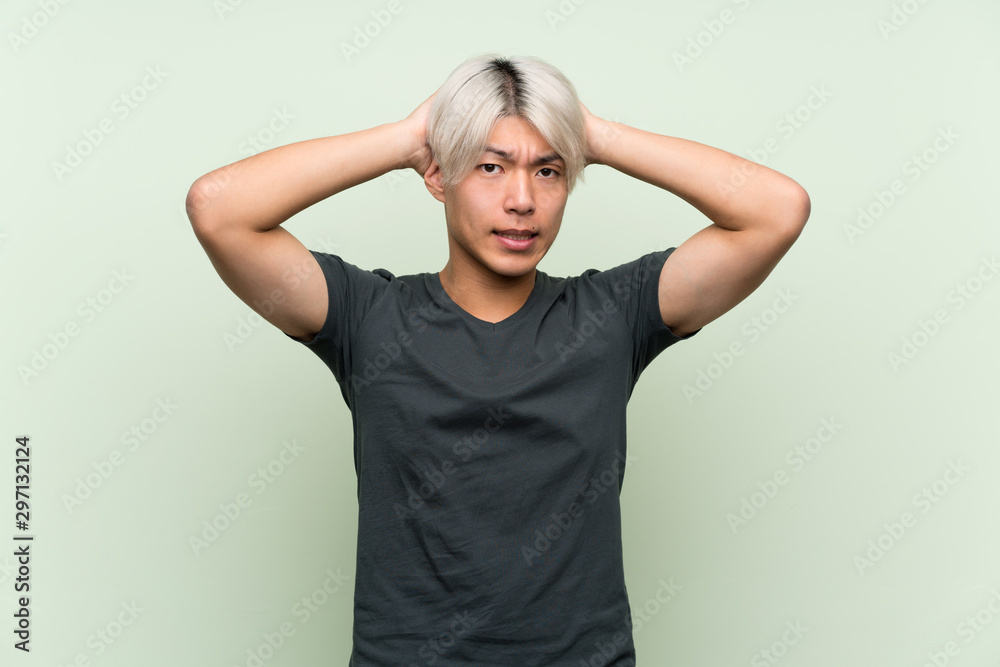 Young asian man over isolated green background frustrated and takes hands on head