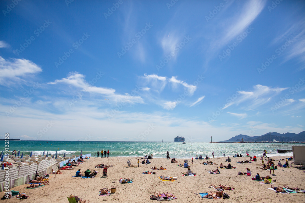 Obraz premium The beach in Cannes. Cannes, France, Cote d'Azur - April 30, 2018: the beach in Cannes. Mediterranean Sea, beach in France. People on the beach, cruise ship in the sea.