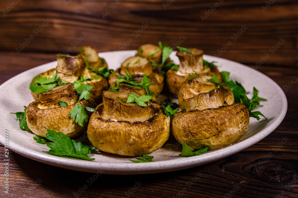 Plate with baked champignons, dill and parsley on a wooden table