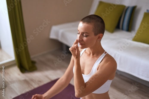 Flexible woman with closed eyes practicing nadi shodhana pranayama (Alternate Nostril Breathing) at home on purple mat. photo
