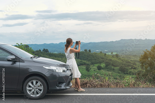 Young woman traveler taking a photo on mountain with car on roadtrip, Summer vacation