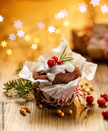 Christmas gingerbread muffin covered with icing decorated with cranberry and rosemary on a wooden table. Delicious dessert