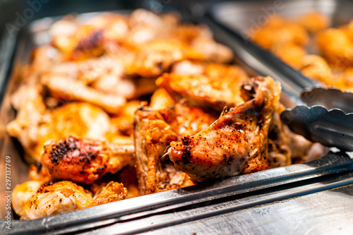 Roasted chicken thighs buffet bar self serve with tongs in grocery store, restaurant or catering event with crisp skin and unhealthy food