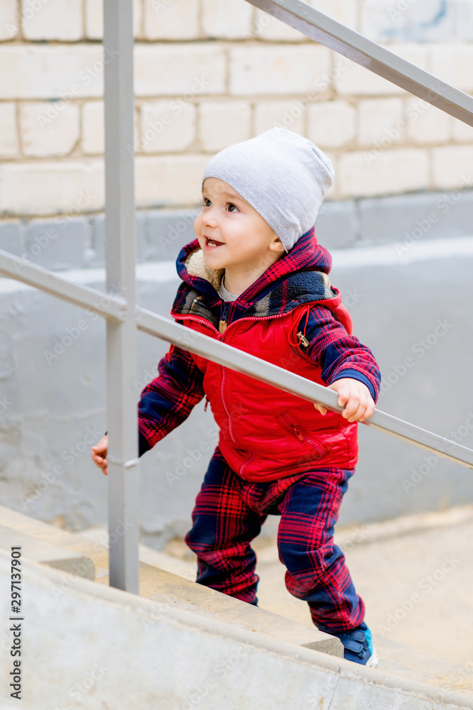 A brightly dressed two-year-old baby is playing on the stairs. He smiles cheerfully. A brightly dressed two-year-old baby is playing on the stairs. He smiles cheerfully.