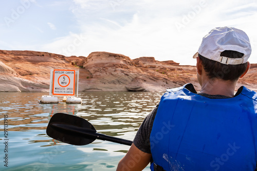 Man kayaking in Lake Powell with view of canyons water and sign for antelope canyon speed limit wake wakeless zone for boats and paddlers photo