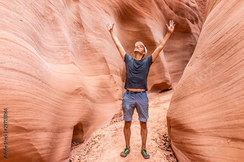 Man happy hiker with arms raised up by red wave shape formations at Antelope slot canyon in Arizona on footpath trail from Lake Powell