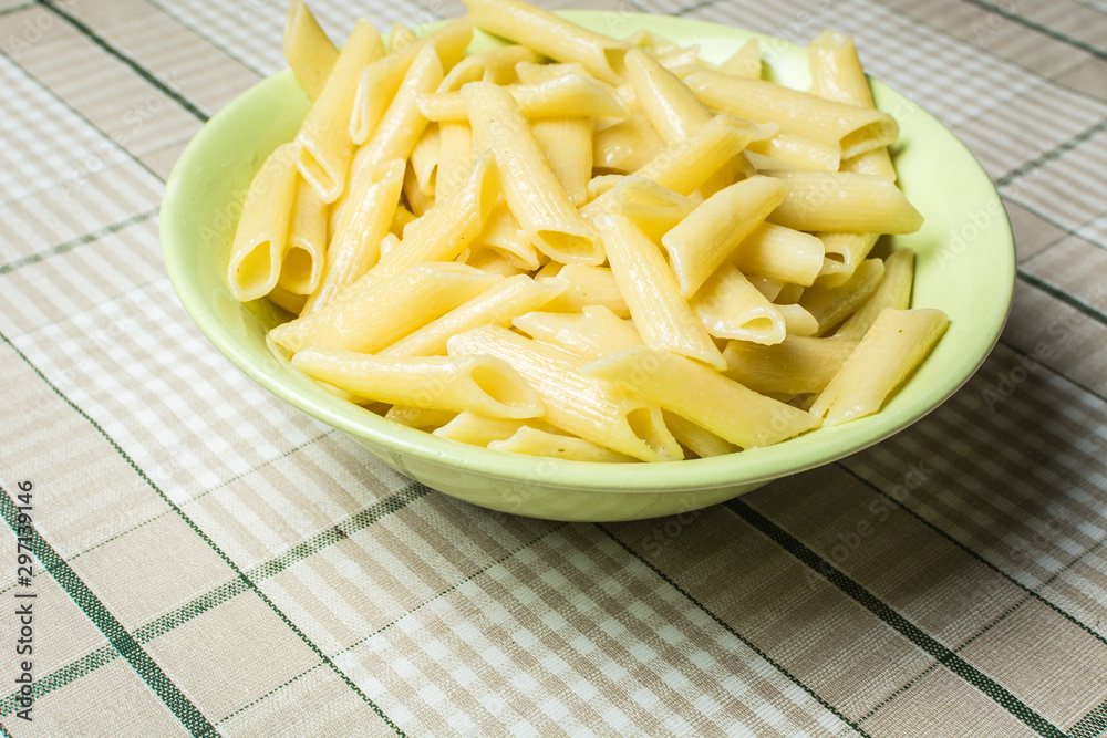Tubular pasta in green plate on kitchen table.