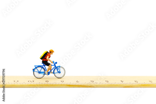 Miniature people ride bicycles on wooden ruler.