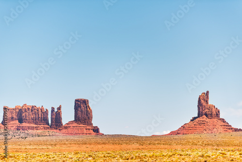 View of many unique cliff mesa formations with red orange rock color on horizon in Monument Valley canyons during summer day in Arizona