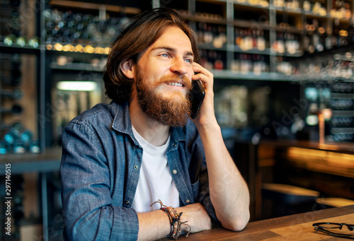 Young bearded brown-haired man talking on mobile phone in a loft cafe