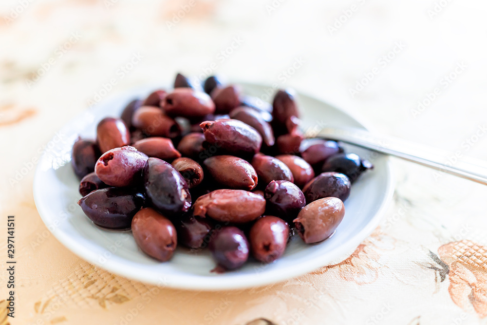 Closeup macro of purple red marinated kalamata olives on white plate in Italy or Greece for serving as appetizer on table party setting Closeup macro of purple red marinated kalamata olives on white plate in Italy or Greece for serving as appetizer on table party setting