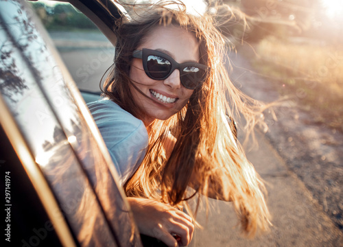 Cute brunette with long fluttering hair leaning out of the window of a car