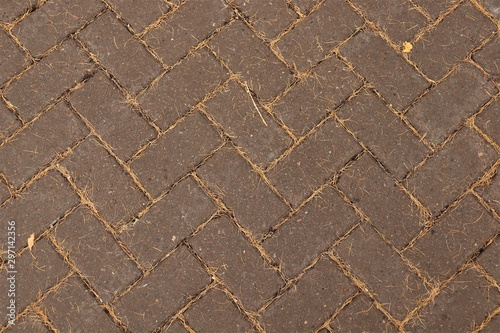 Paving slabs of brown color, between which lie yellow needles of larch.
