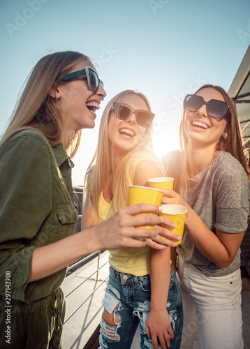 Smiling pretty women in sunglasses drinking on a sunny balcony