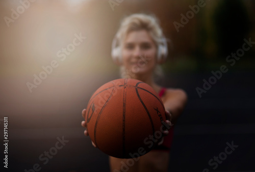 Portrait of a gorgeous concentrated beautiful strong athletic woman outdoors posing while listening to music with headphones holding a basketball.healthy lifestyle concept, sporty girl