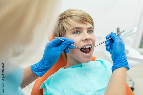 Blonde dentist examines the boy's teeth with a mouth mirror and dental probe